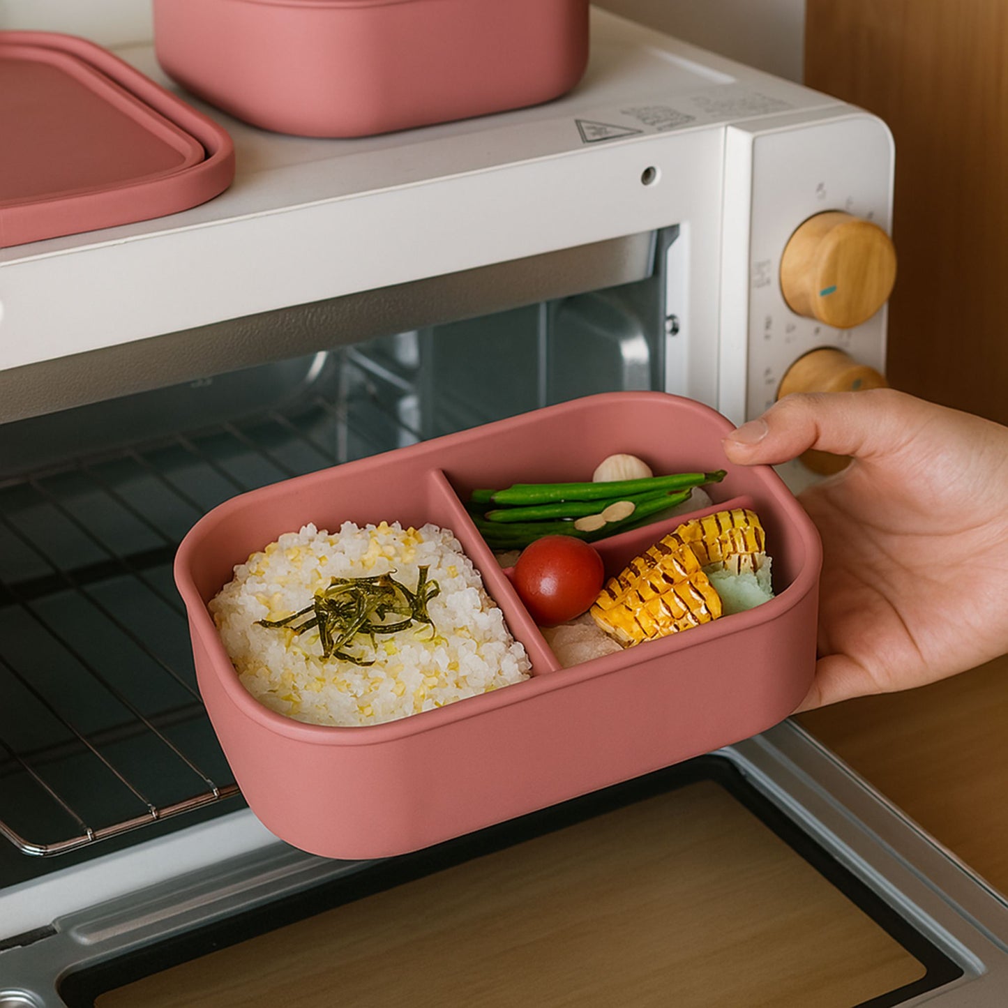 ZipNow silicone everyday lunch box with compartments placed in front of oven with rice and vegetables — ideal for reheating meals.