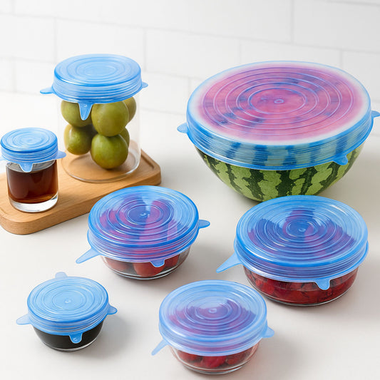 Multiple containers including a halved watermelon and fruit bowls covered with bright blue ZipNow stretch lids, neatly arranged on a white kitchen counter.
