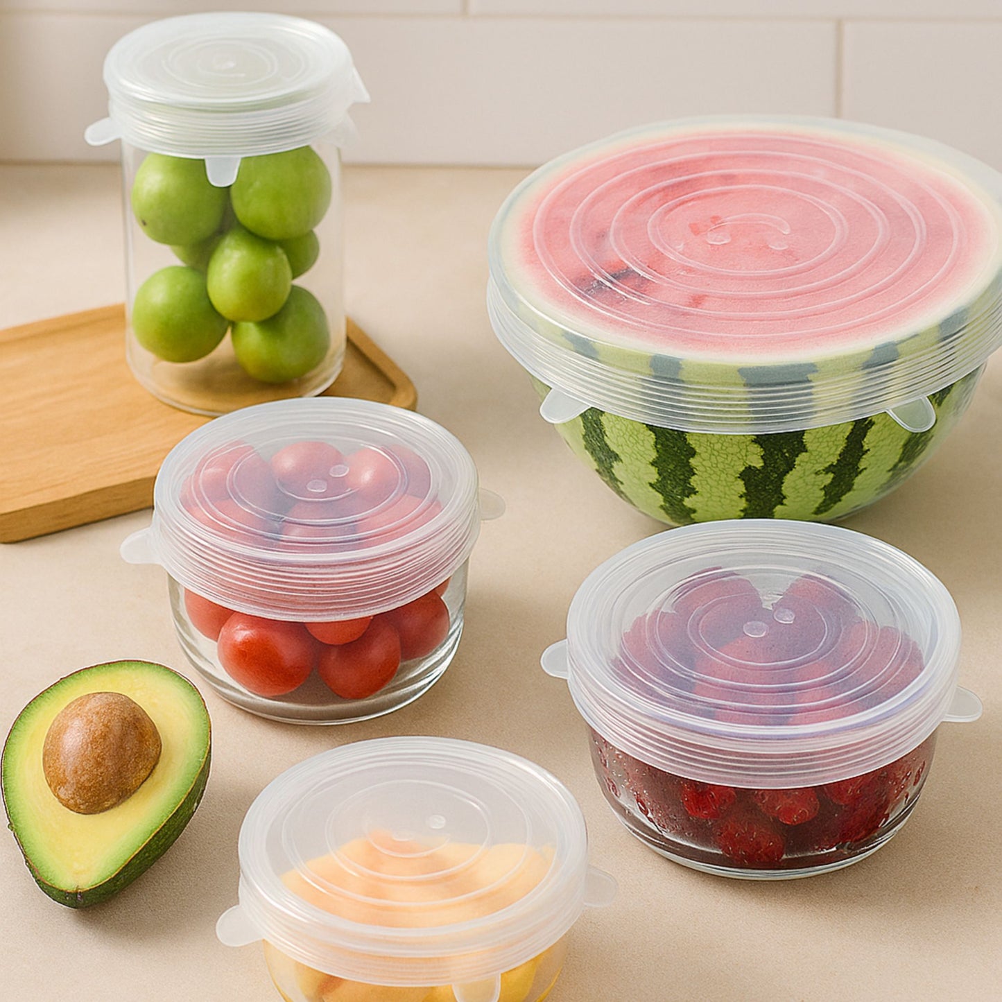 Various fresh fruits like watermelon, tomatoes, and grapes stored in transparent containers sealed with clear ZipNow stretch lids on a beige kitchen counter.
