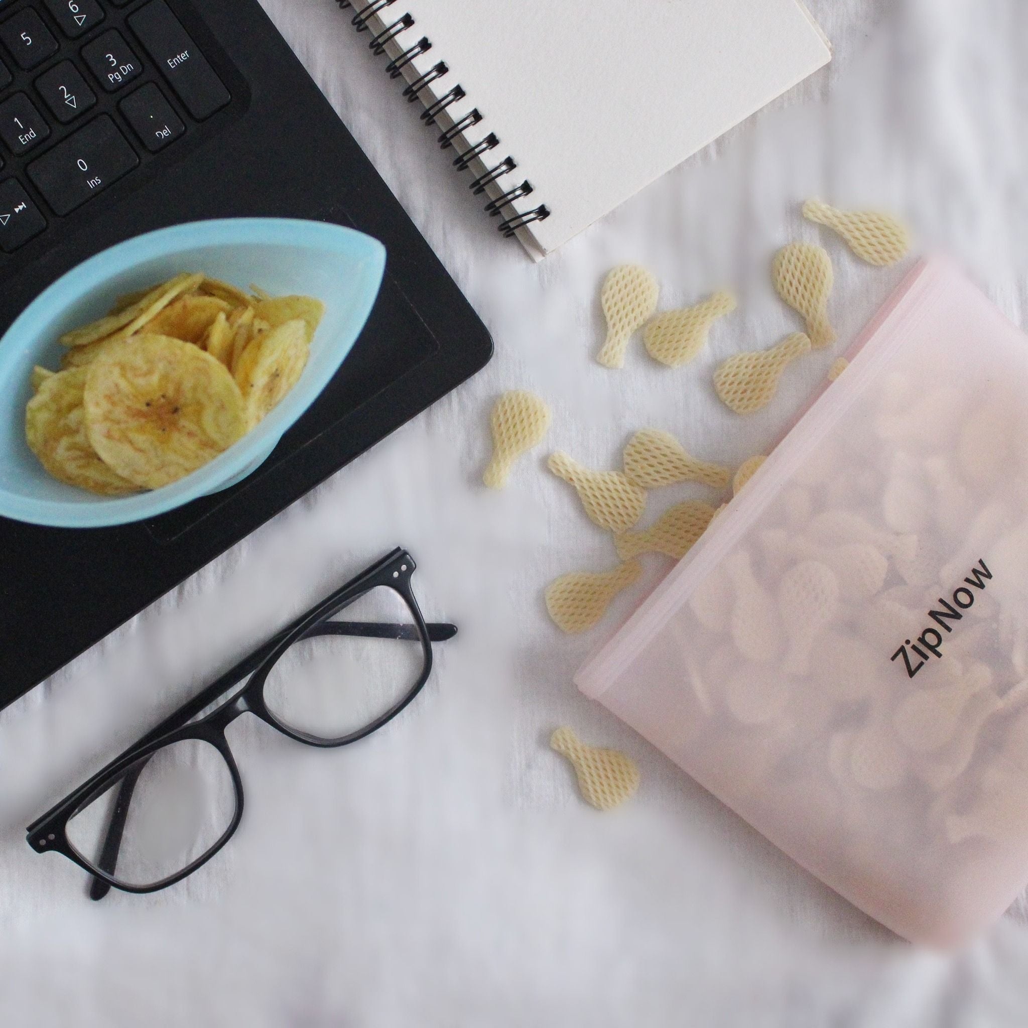 ZipNow Silicone Lifestyle Bag filled with snacks next to laptop and notebook - perfect for work desk