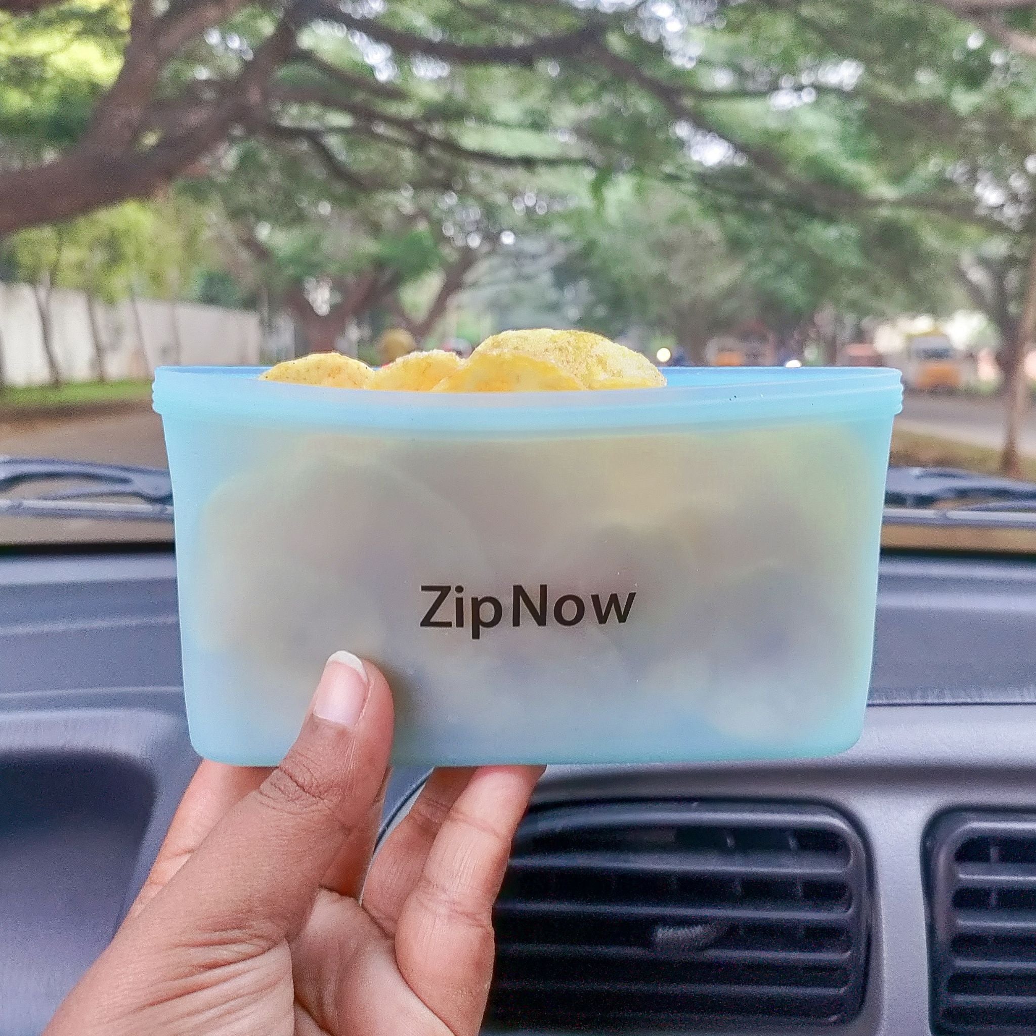Holding ZipNow Silicone Lifestyle Bag filled with chips during a road trip - perfect for travel snacks