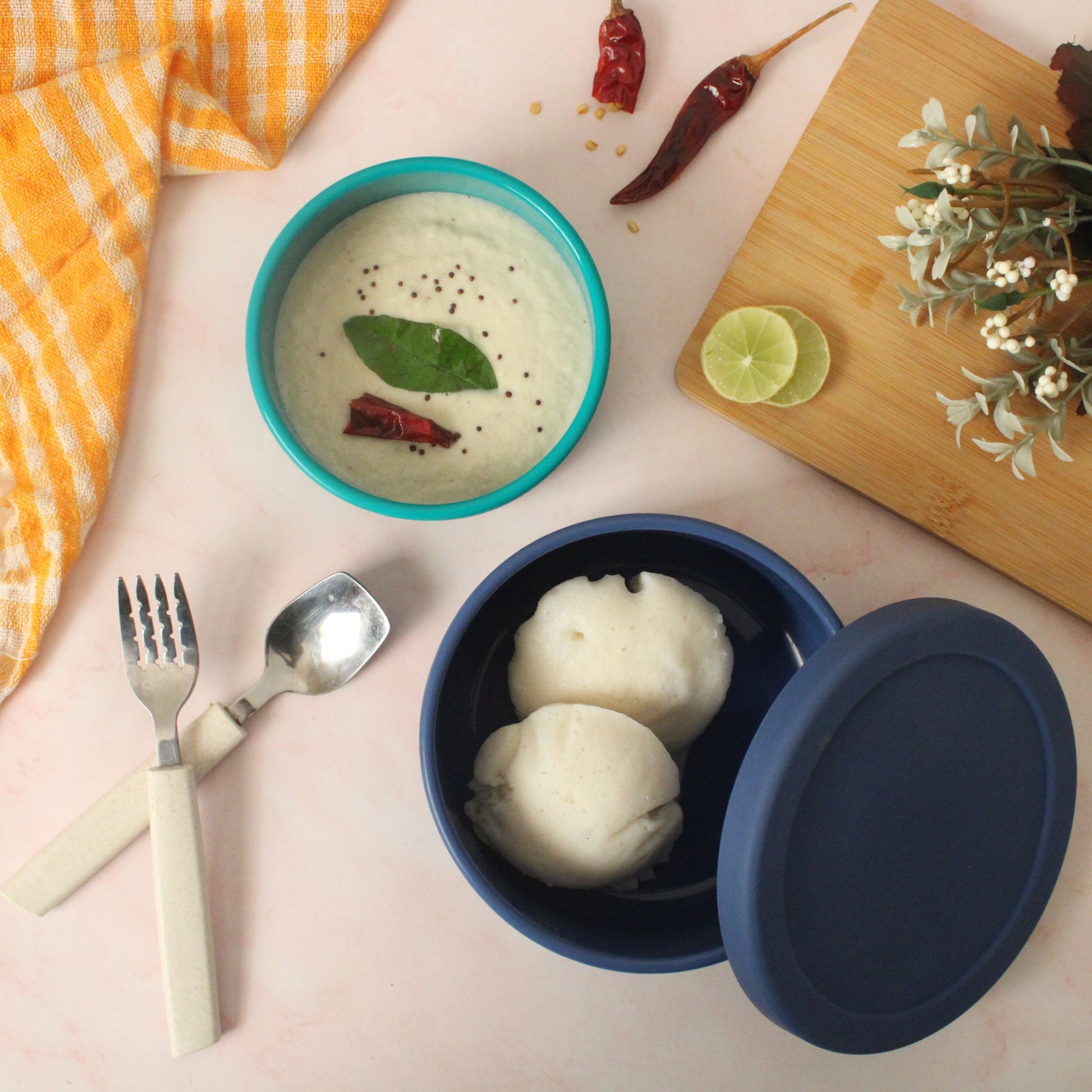 Blue and green ZipNow round containers used to serve idli and chutney on a breakfast table.

