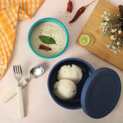 Blue and green ZipNow round containers used to serve idli and chutney on a breakfast table.
