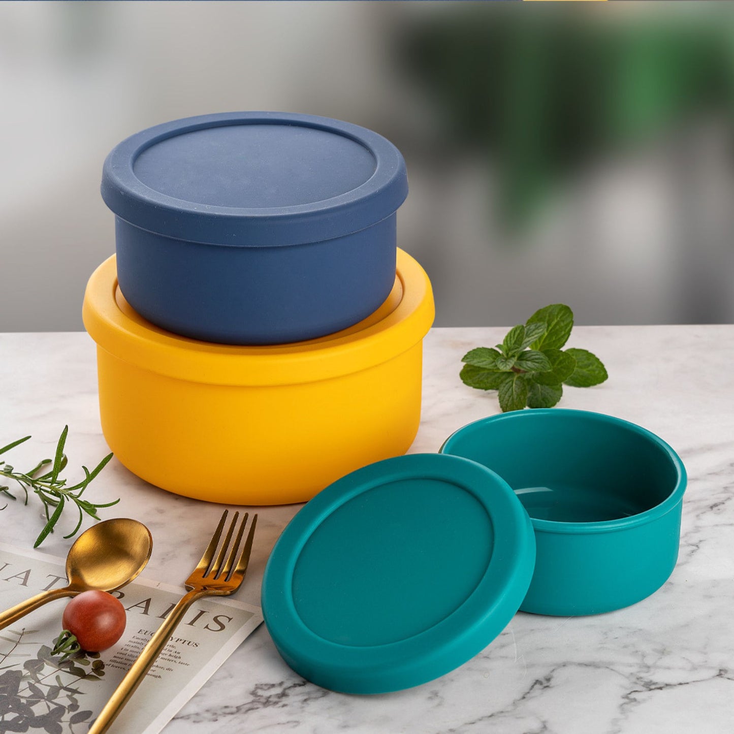Modern marble kitchen setup featuring stacked silicone round containers in blue, yellow, and teal.
