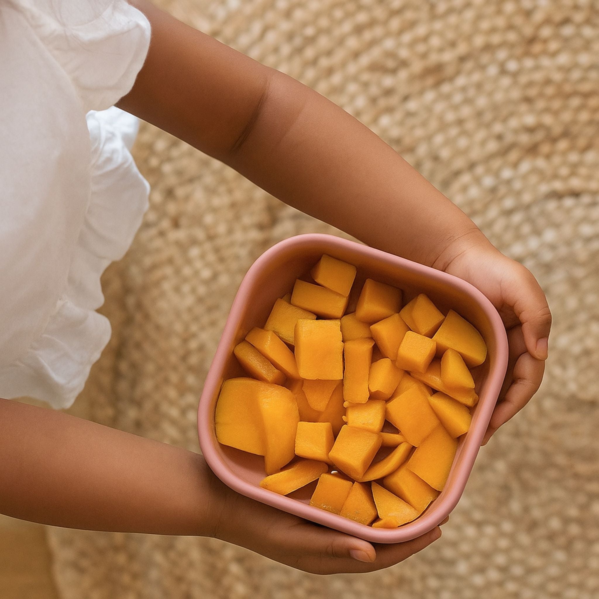 Child holding a pink ZipNow silicone container filled with fresh mango cubes
