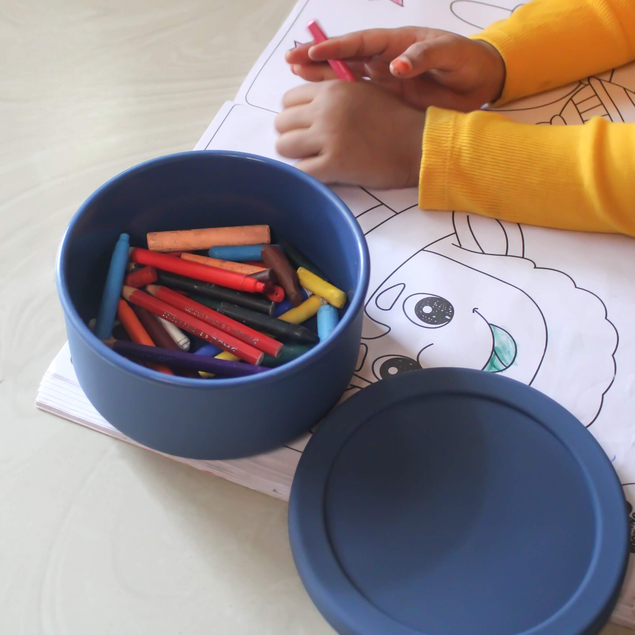 ZipNow Silicone Round Blue container with colorful crayons next to a child coloring a picture
